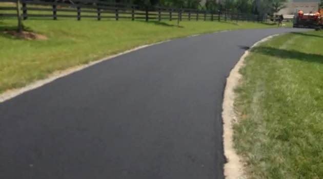 Wide black asphalt drive bordered by green lawn and fencing