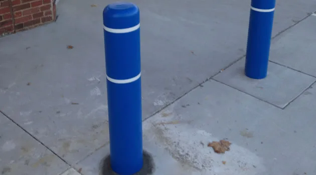 Freshly painted blue protective bollard set in asphalt