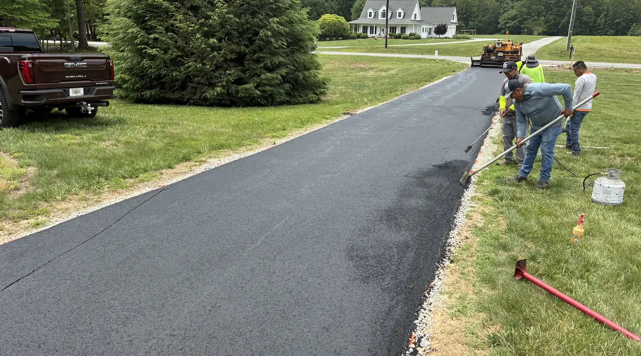 Crew hand-raking the edge of a freshly paved asphalt driveway