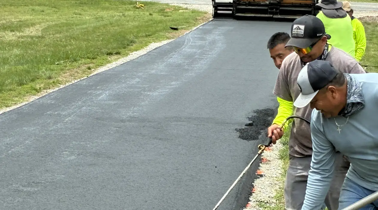 Paving crew tacking and finishing the edge of fresh hot asphalt