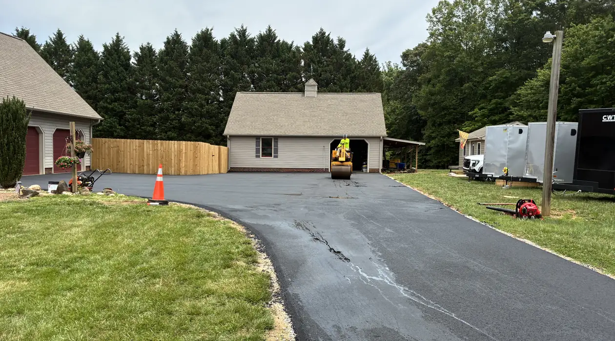 Roller compacting a freshly paved driveway in front of a garage