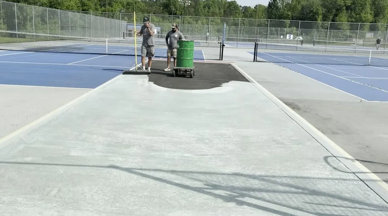 Crew squeegeeing resurfacer over a repaired court section
