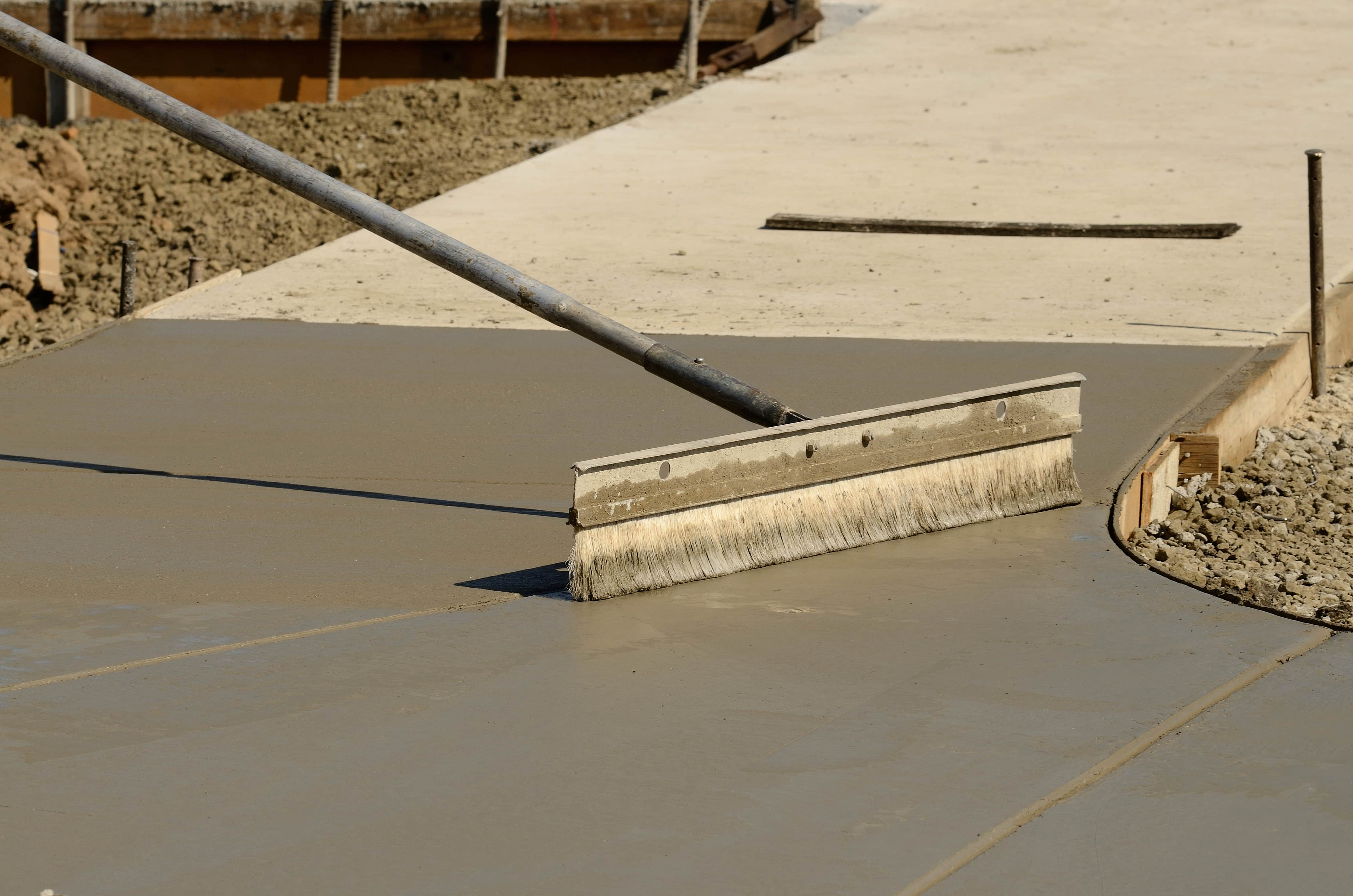Concrete mason contractor using finishing broom to texture a new sidewalk at a new commercial residential development project