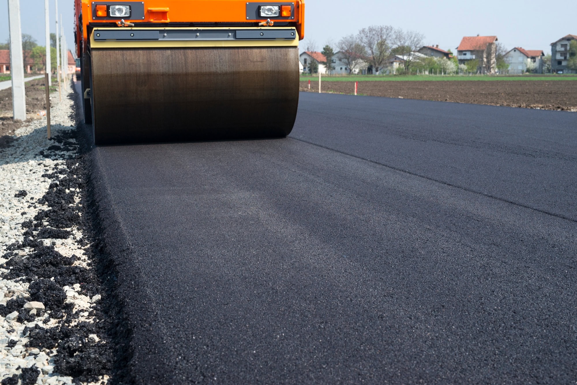 A chip sealer is seen sealing fresh asphalt chips during the day time.